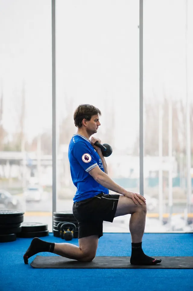 Kmover en posición de rodilla con kettlebell junto al ventanal
